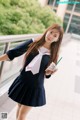 A woman in a school uniform holding a drink.