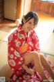 A woman in a red kimono sitting on the floor.