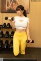 A woman in a white top and yellow leggings holding two dumbbells.