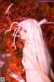 A woman with long pink hair standing in front of a tree.