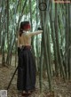 A woman in a black dress holding a sword in a bamboo forest.