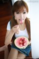 A young woman eating a slice of watermelon with a spoon.