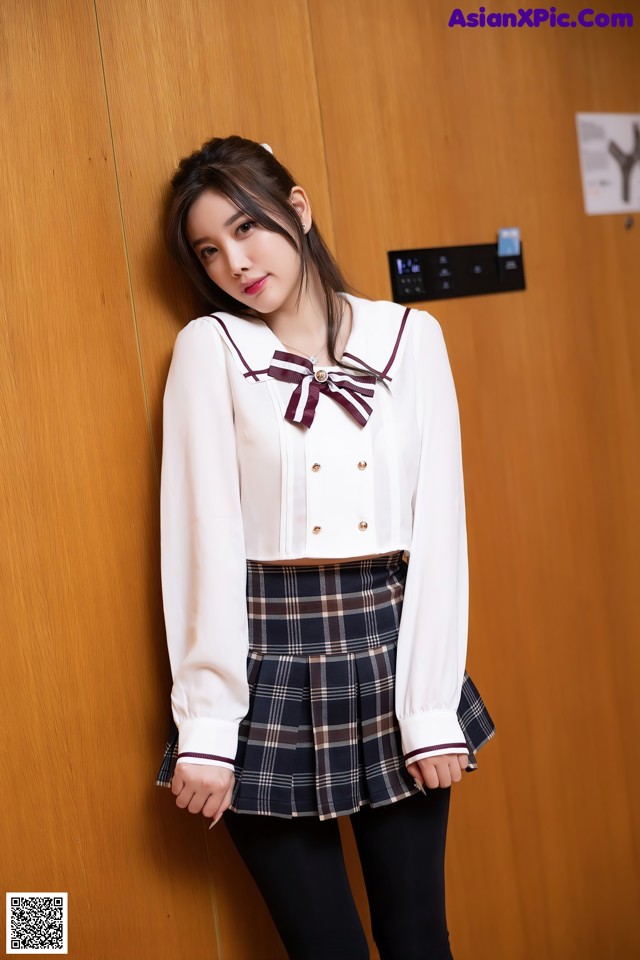 A woman in a school uniform leaning against a wooden wall.