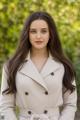 A woman in a beige trench coat posing for a picture.